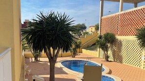 Uma área de piscina com duas piscinas, palmeiras e um edifício com fachada treliçada.