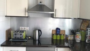 Cozinha com armários brancos, bancada preta, fog ão a gás, cafeteira e recipientes verdes.