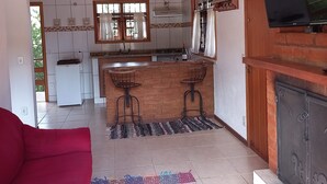 Een gezellige woonkamer met een rode bank, een keuken met een houten bar en een televisie bevestigd aan een bakstenen muur.