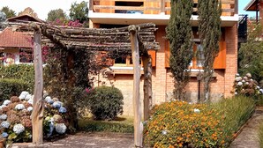 Een traditioneel houten huis met een balkon, omringd door een tuin vol bloemen en struiken.