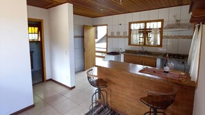 Een keuken met een houten plafond, betegelde vloer en een bar met krukken.