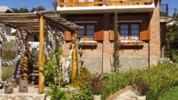 Een houten huis met twee verdiepingen en een balkon, omgeven door een tuin met verschillende planten en een pad van stenen.