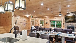 A wooden interior with a dining area, a fireplace, and a stone accent wall. - Luxury Gatlinburg Cabin w/ Indoor Pool + Theater + 2 Hot Tubs | Sleeps 24 (Gatlinburg)