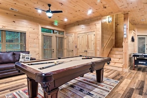 Relax in a cozy space with a pool table, leather sofa, and staircase leading to an upper level.