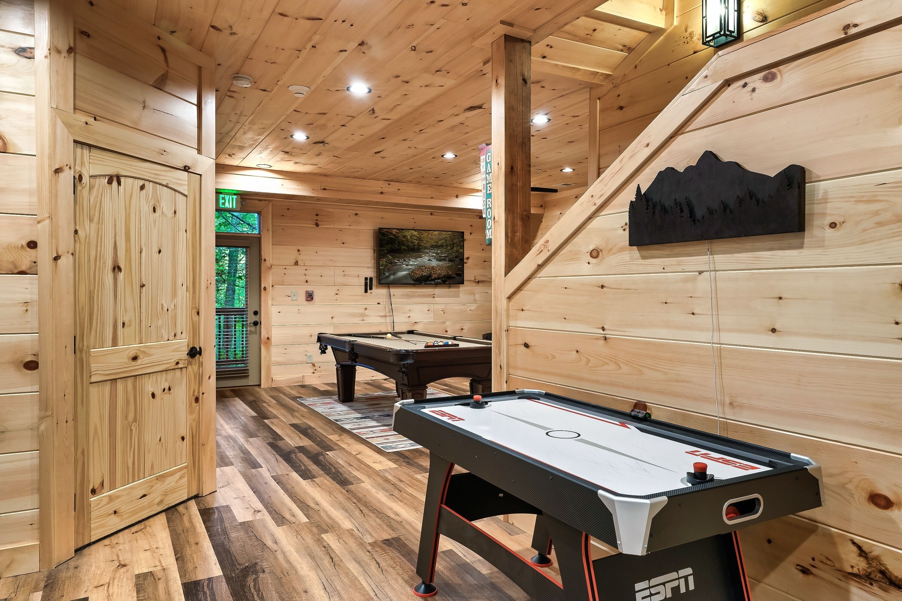 Un interior de madera con mesa de billar, mesa de hockey de aire y un mural en la pared.
