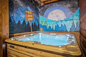 Relax in the hot tub under a starry night sky, surrounded by a serene forest scene.