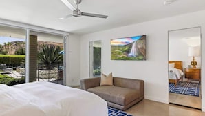 A hotel room with a bed, a sofa, a TV, a ceiling fan, and a large window with a view of a garden and mountains. - Mod Blue Agave - Stunning S Palm Springs Mid-Centu (Palm Springs)