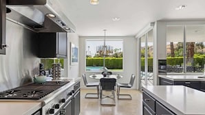 A modern kitchen with a gas stove, stainless steel cabinets, and a dining area with a round table and chairs. - Mod Blue Agave - Stunning S Palm Springs Mid-Centu (Palm Springs)
