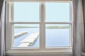 Una ventana con vista a un muelle que se adentra en el agua, rodeado de vegetación.