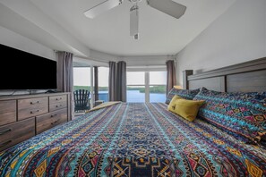 Un dormitorio con una cama grande, televisor, una silla y vistas al exterior.