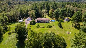 A large house surrounded by a forested area with a swimming pool and a well-maintained lawn.
