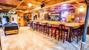 A bar area with a pool table, bar stools, and a variety of bottles.