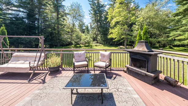 A deck with a glass-top table, two cushioned chairs, a swing chair, and a wood-burning stove.