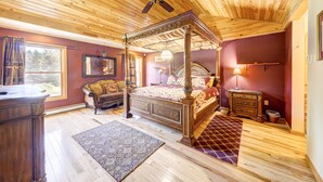 A spacious bedroom with a four-poster bed, a wooden ceiling fan, a large window, and a view of the outdoors.