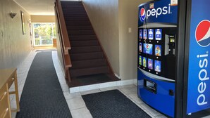 Un couloir avec un escalier, un distributeur de boissons Pepsi et un banc en bois.