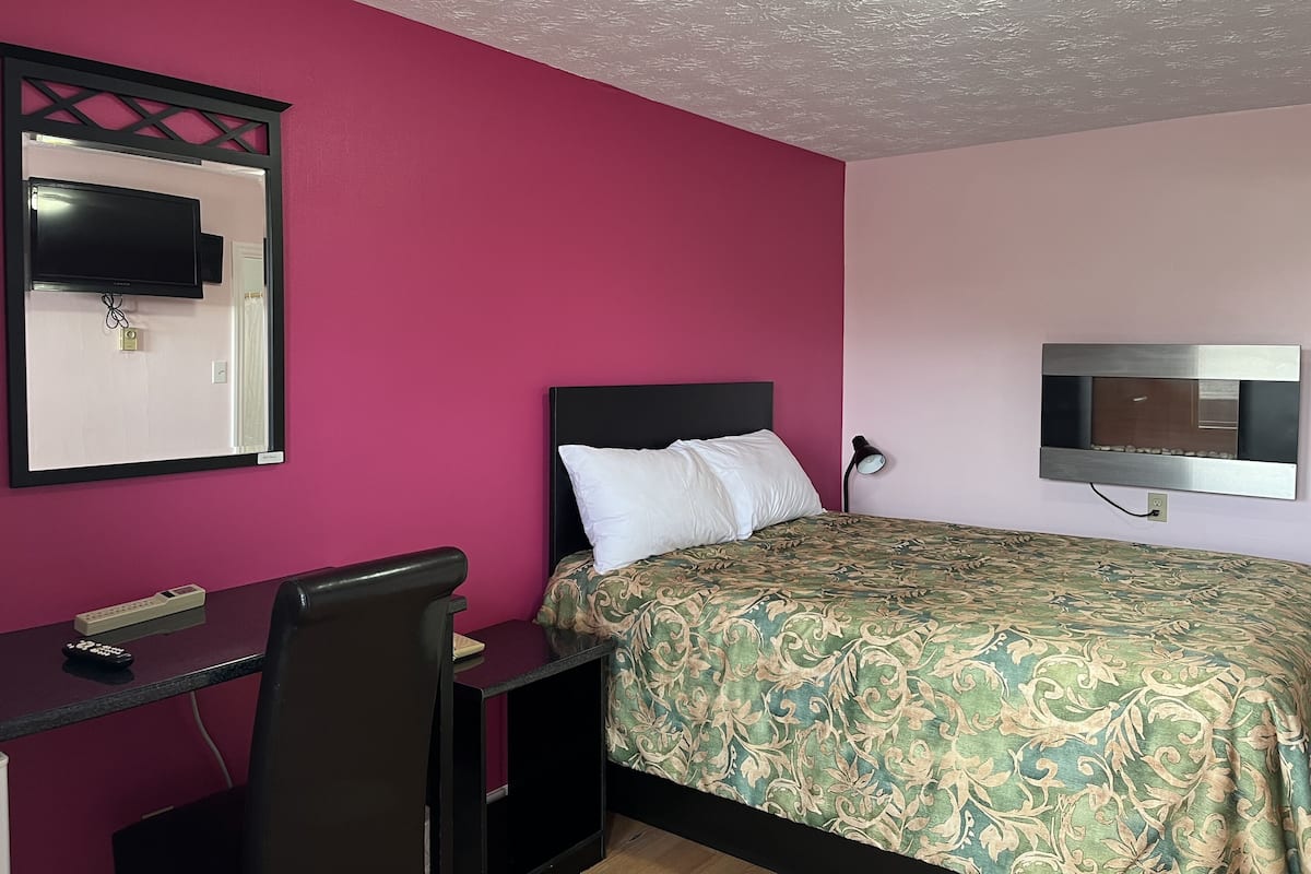 A room with a bed, a desk, a chair, a TV mounted on the wall, and a ceiling light.