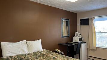A hotel room with a bed, a desk with a telephone, a coffee maker, and a window with curtains.