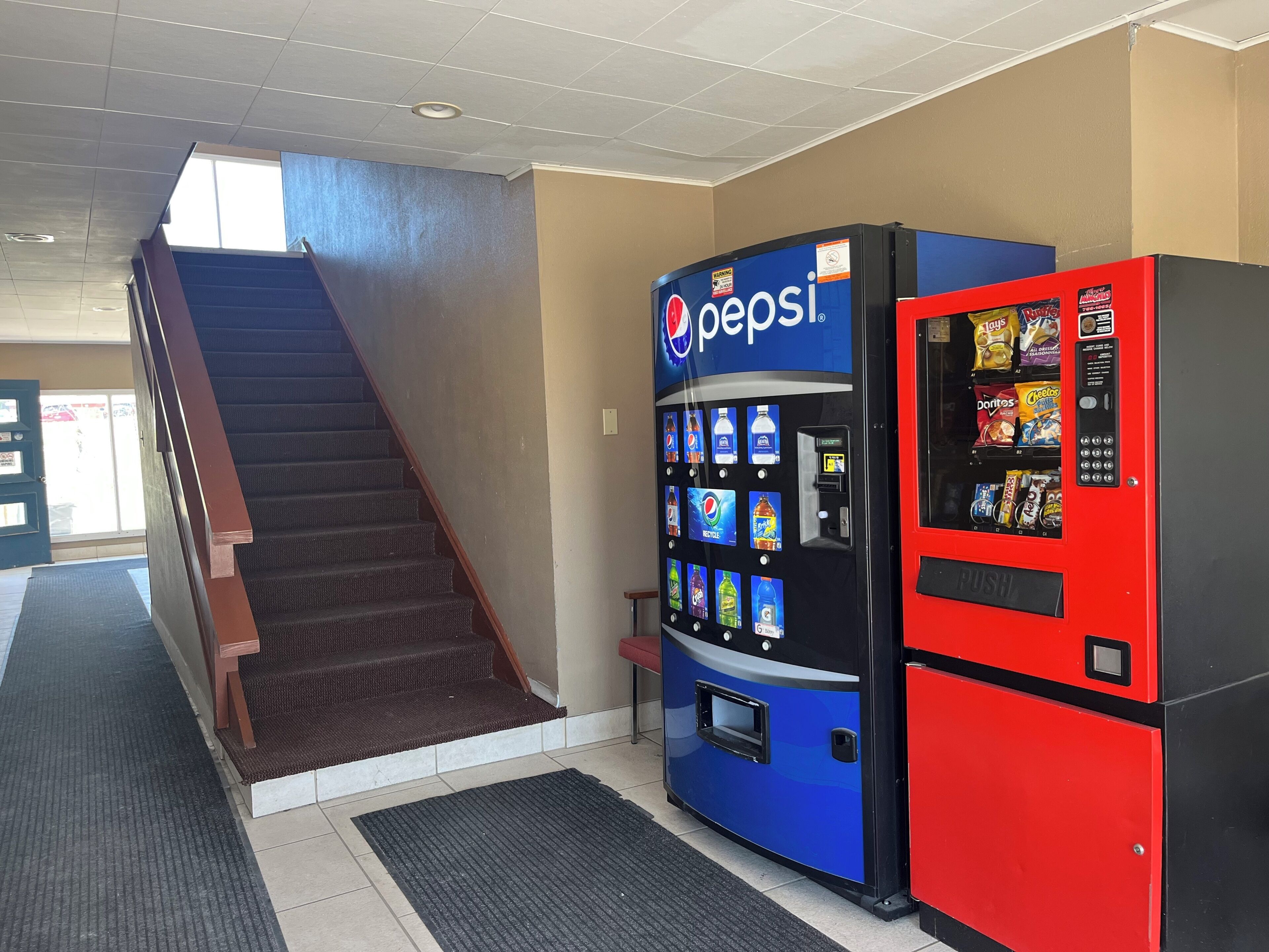 A vending machine with Pepsi branding, a staircase, and a red vending machine with snacks.