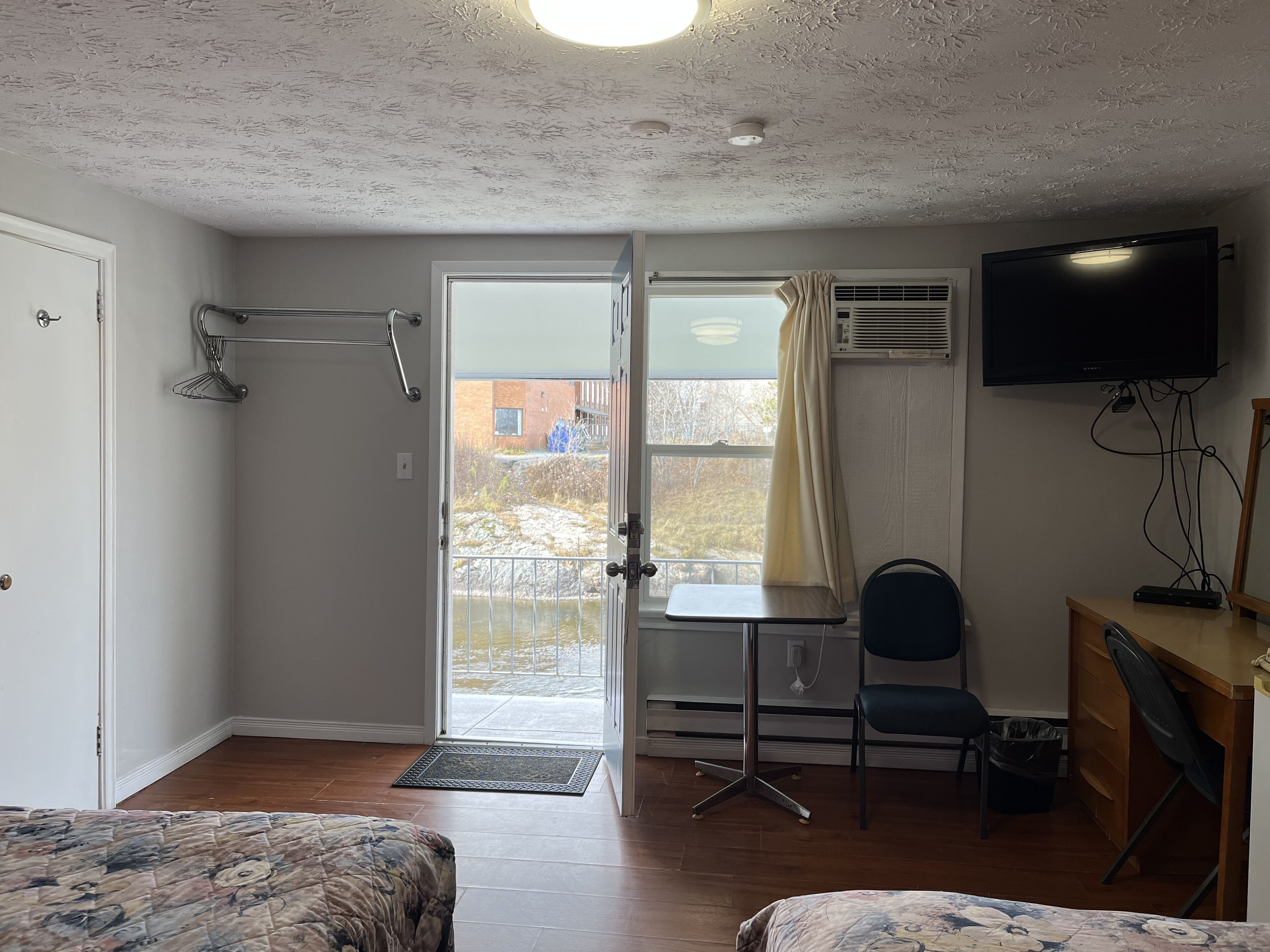 A room with a bed, a desk, a chair, a TV, and a door leading to a balcony.