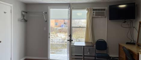 A room with a bed, a desk, a chair, a TV, and a door leading to a balcony.