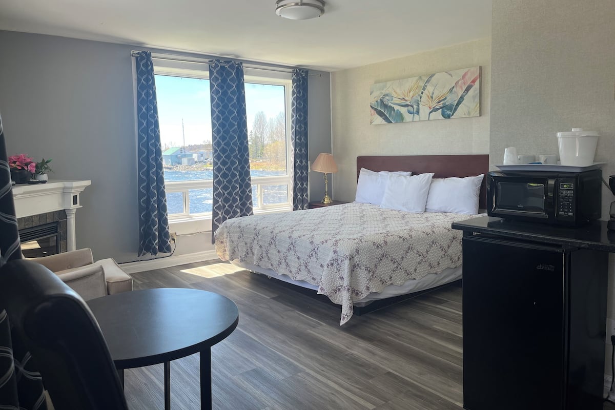 A hotel room with a bed, a desk, a chair, a microwave, a lamp, and a painting on the wall.
