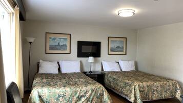 A hotel room with two single beds, a flat-screen TV, a standing lamp, and two framed pictures on the wall.
