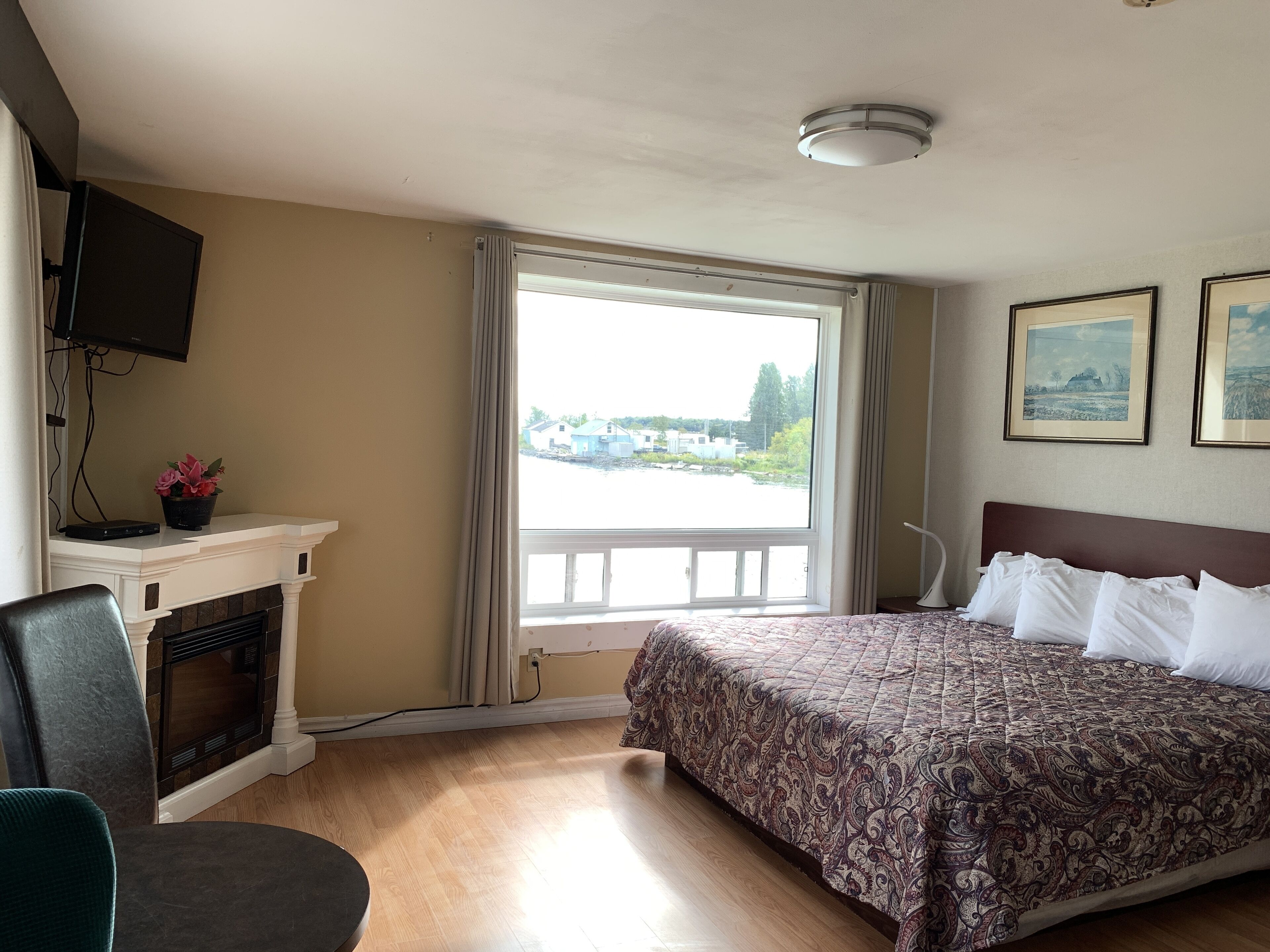 Habitación de hotel con cama, televisor montado en la pared, chimenea y ventana con vistas a edificios.