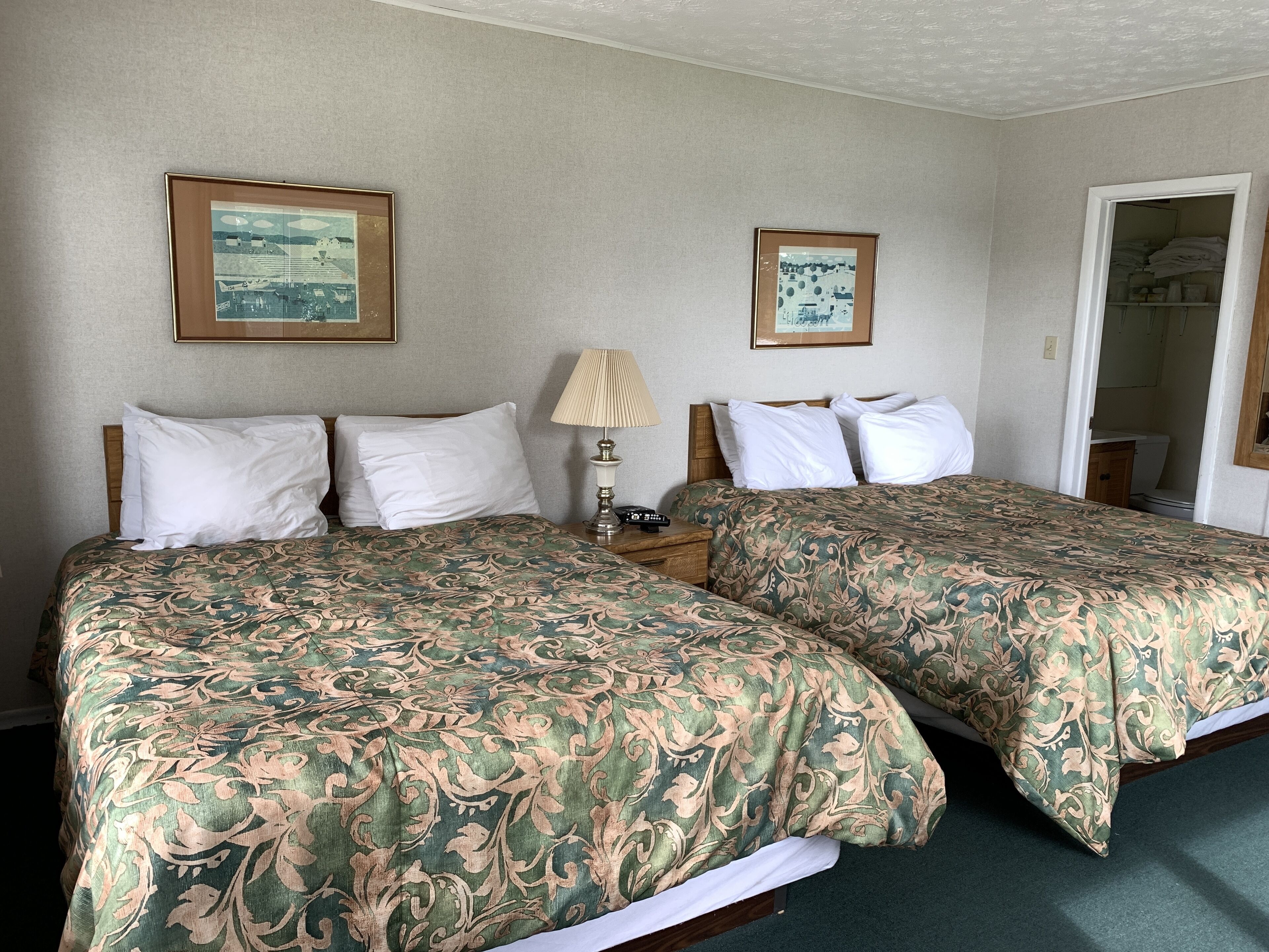 Une chambre d’hôtel avec deux lits, chacun recouvert d’une couvre-lit à motifs, une table de chevet avec une lampe et des tableaux encadrés accrochés au mur.