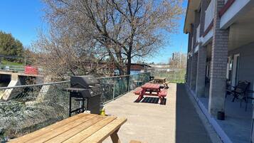 Un patio con una parrilla, mesas de picnic y vistas de un río y edificios.