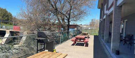 A patio with a grill, picnic tables, and a view of a river and buildings.