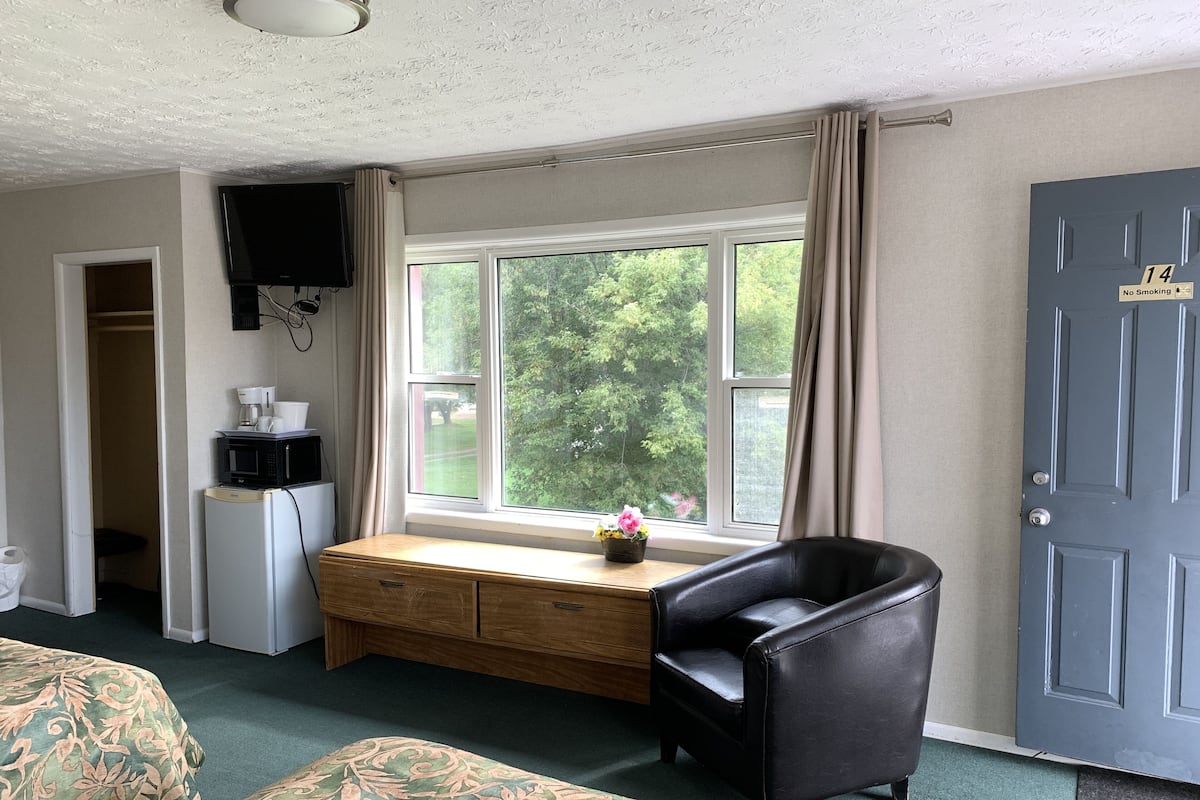 A room with a bed, a desk with a chair, a television, a refrigerator, and a window with curtains.