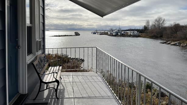 Un balcon avec un banc, donnant sur une rivière où l’on aperçoit des bateaux et des bâtiments au loin.