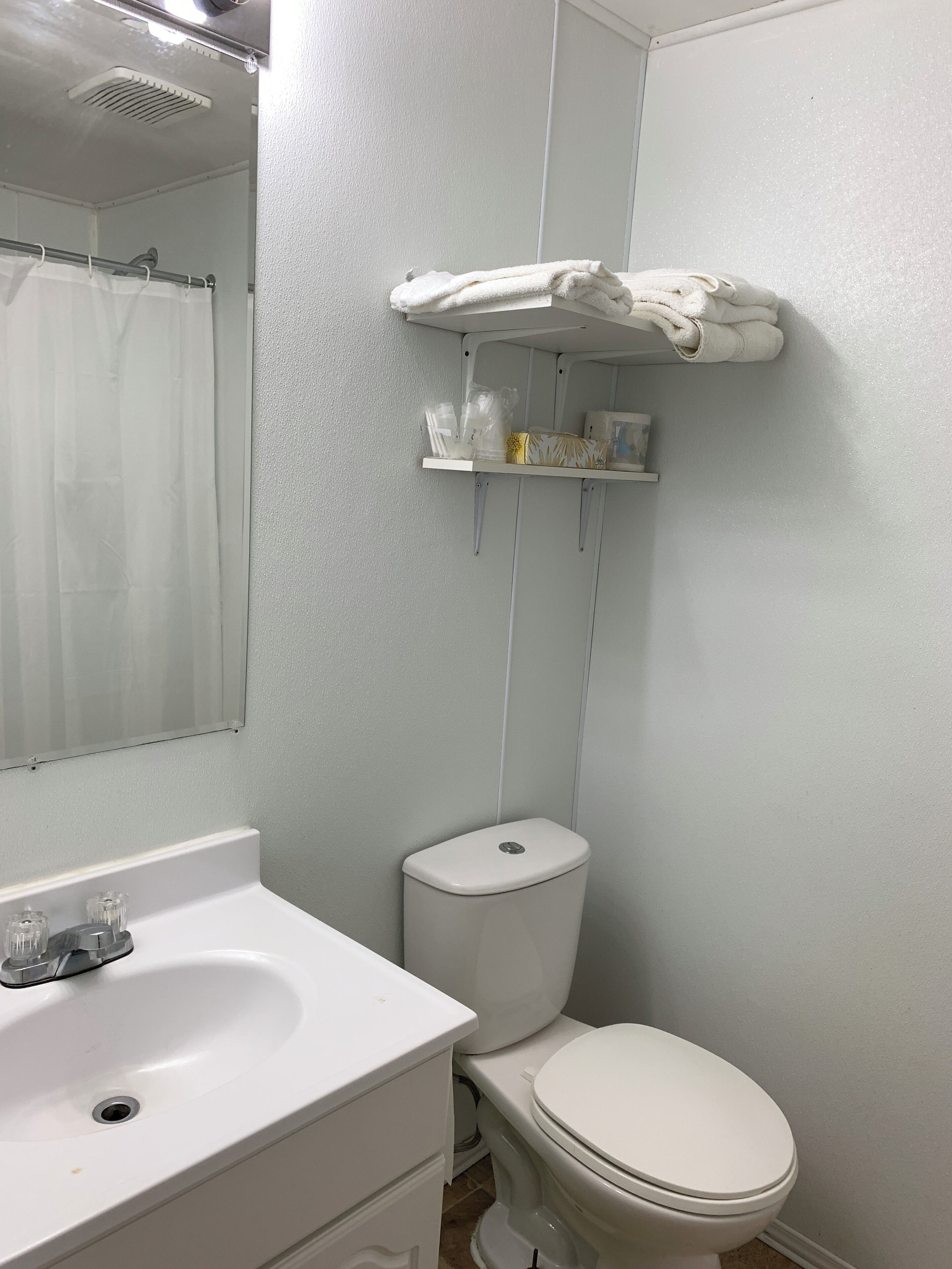 Un baño con lavamanos blanco, inodoro y un perchero con toallas dobladas.