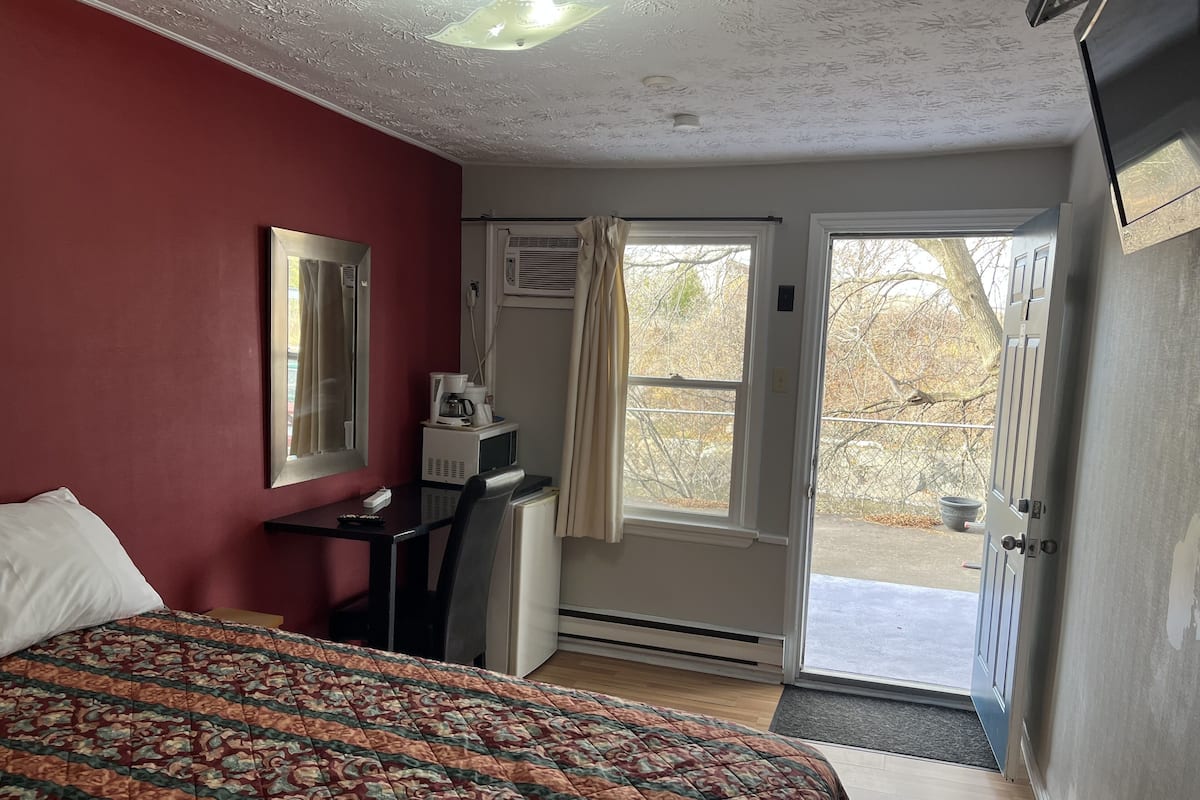 A bedroom with a bed, a desk with a computer, an air conditioning unit, and a door leading outside.