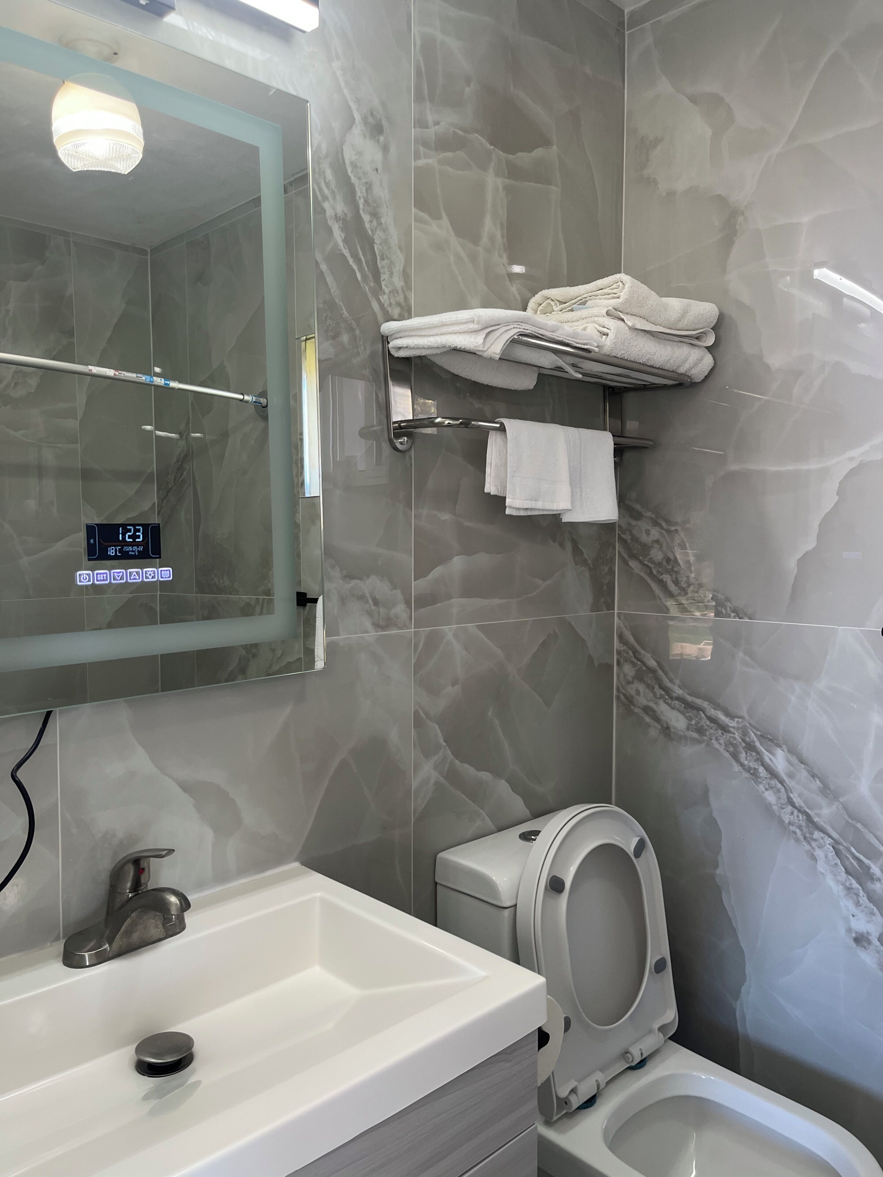 Ein Badezimmer mit Marmorwand, einem Waschbecken mit Wasserhahn, einer Toilette und einem Handtuchhalter mit gefalteten Handtüchern.