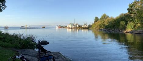 A calm river with a fishing chair and gear on a rocky shore.