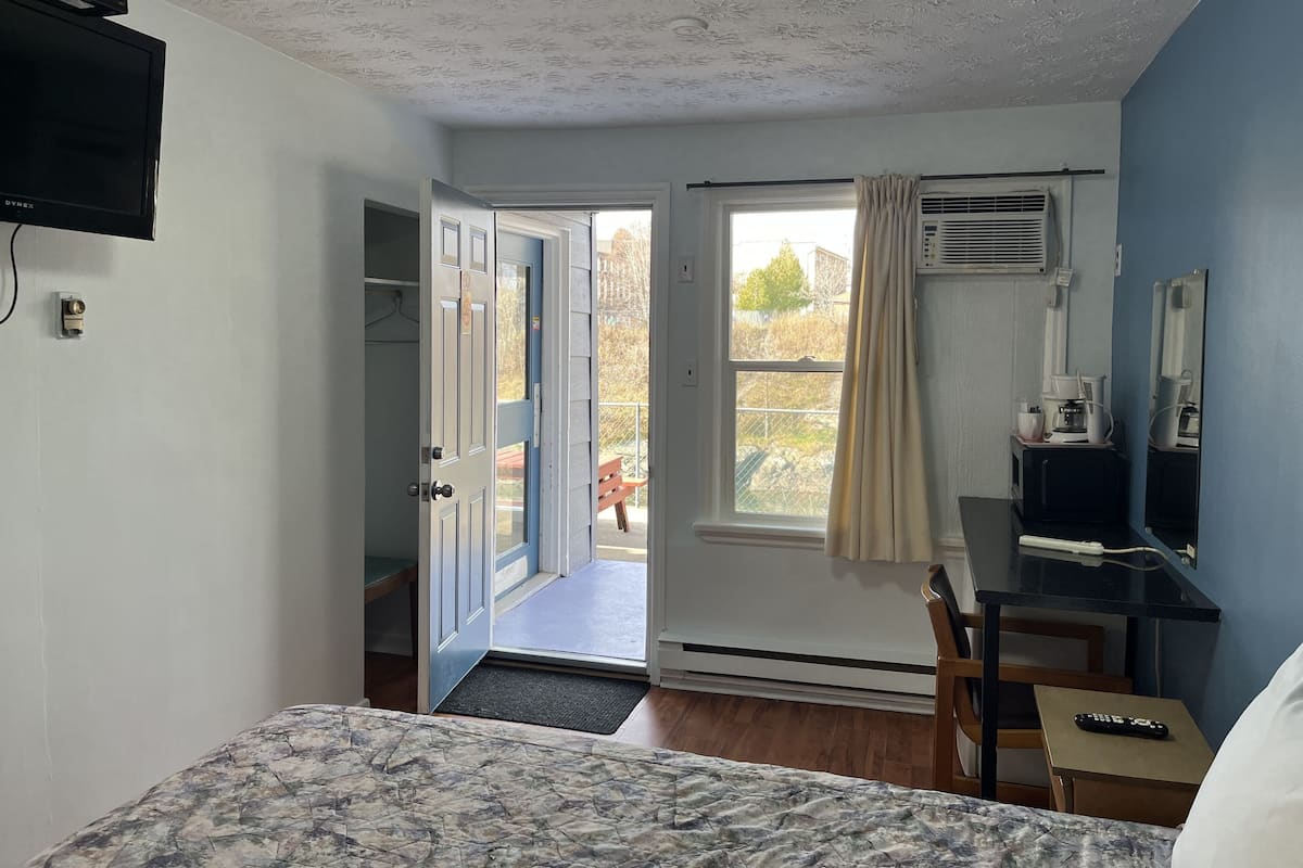 A room with a bed, a desk with a computer, a TV, and a window with curtains.