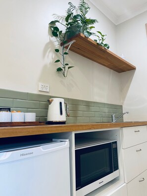Una cocina con encimera de madera, un electrodoméstico blanco con la etiqueta 'Hisense', un horno microondas y una estantería de madera con una planta.