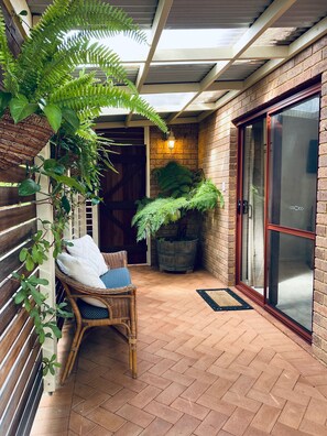 A covered patio area with a wicker chair, a potted plant, and a sliding glass door.