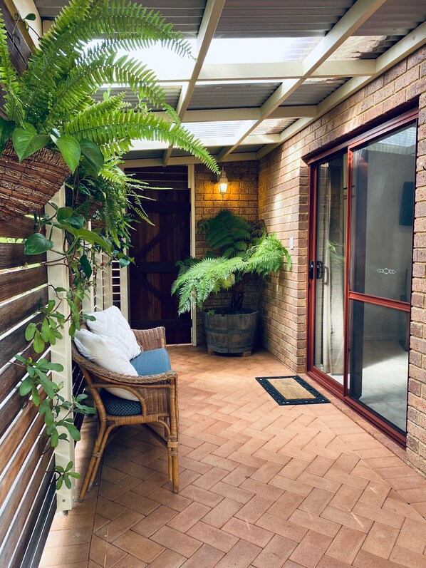 A covered patio area with a wicker chair, a potted plant, and a sliding glass door.