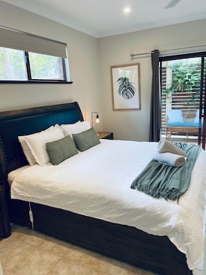 A neatly made bed with pillows and a blanket, a bedside lamp, and a framed plant on the wall.