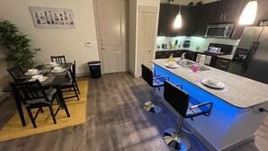 Una cocina moderna con una isla central, armarios oscuros y un comedor con una mesa y sillas de madera.