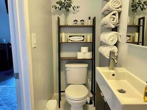 Bathroom with a toilet, sink, and toiletries on a shelf.