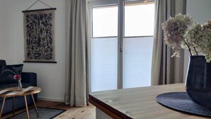 A modern living room with a wooden coffee table, a round rug, a sofa, and a large window with curtains. - Vacation apartment Breitenberg approx. 50 sqm (Rottau)