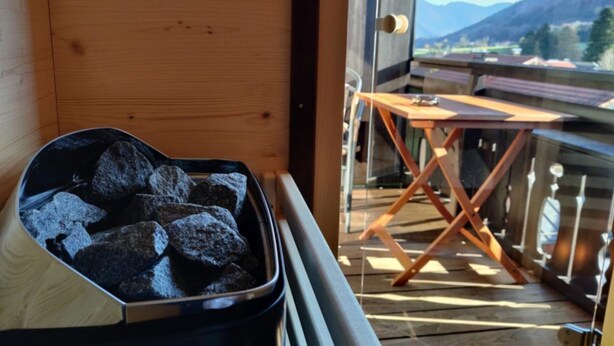 A balcony with a view of mountains, a wooden door, and a table with a chair. - Vacation apartment Breitenberg approx. 50 sqm (Rottau)
