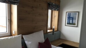 Un dormitorio con cabecera de madera, cama con ropa de cama blanca y almohadas rojas, un banco y una ventana con vistas al exterior.