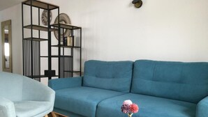 Un salón con un sofá azul, un sillón azul claro y dos mesitas de madera.