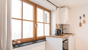 A modern kitchen with a window, white cabinets, a stove, and a microwave. - Vacation apartment Steinröschen 30 sqm, 1 separate bedroom (Reit im Winkl)