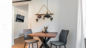 A dining area with a wooden table, two grey chairs, a hanging pendant light, and a small vase with flowers. - Vacation apartment Steinröschen 30 sqm, 1 separate bedroom (Reit im Winkl)