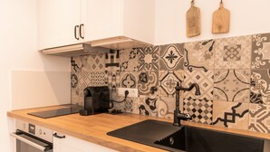 A kitchen with a wooden countertop, black sink, and patterned backsplash. - Apartment Enzian 32 sqm with balcony, 1 separate bedroom (Reit im Winkl)